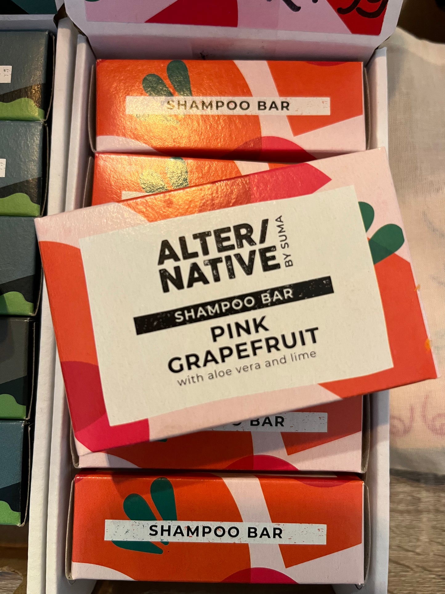A brightly coloured rectangular cardboard box holding a Shampoo bar scented with Pink Grapefruit, Aloe Vera and Lime.