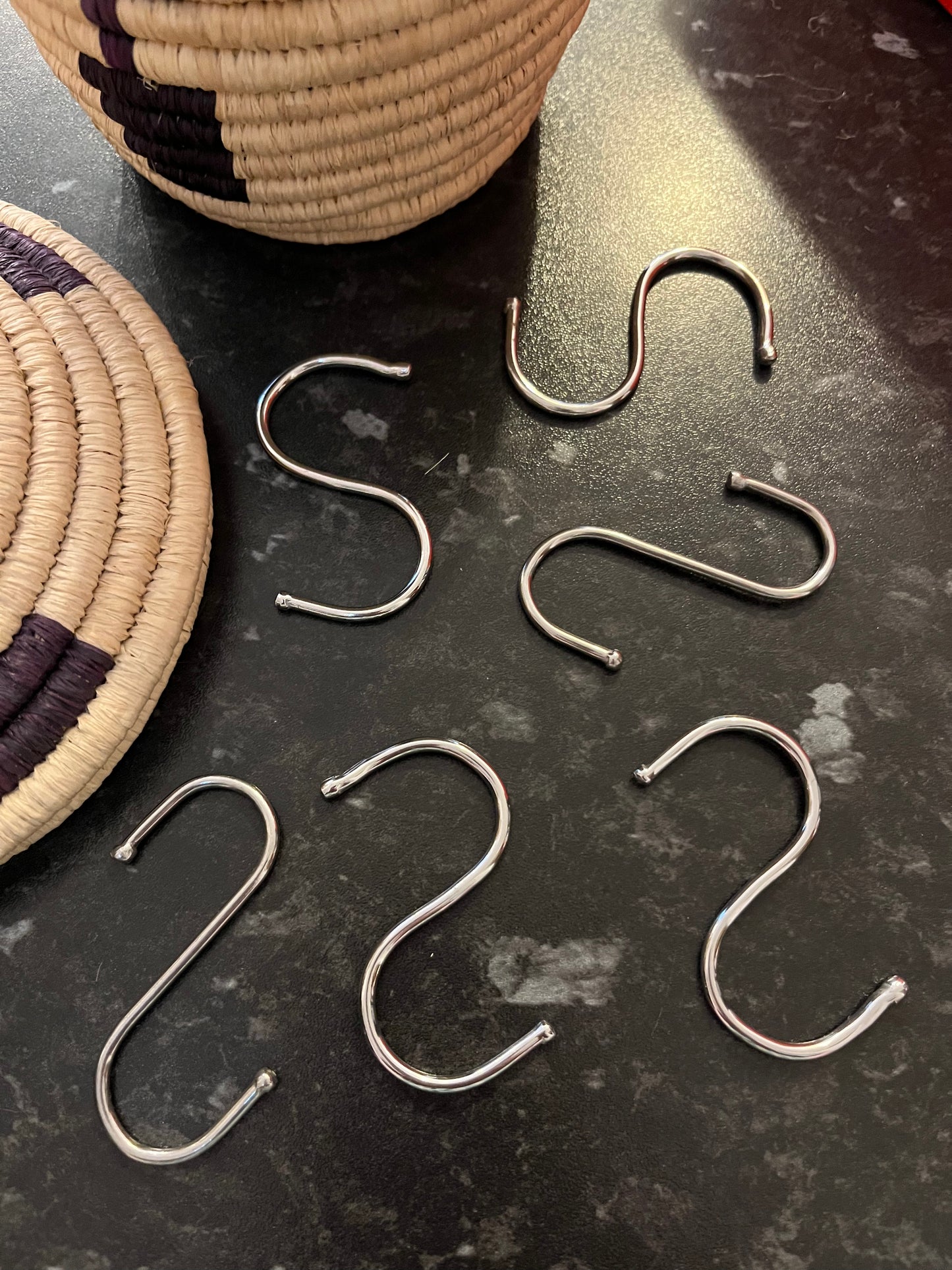 Several S shaped hooks made from a silver coloured metal lie next to a basket on a dark surface.