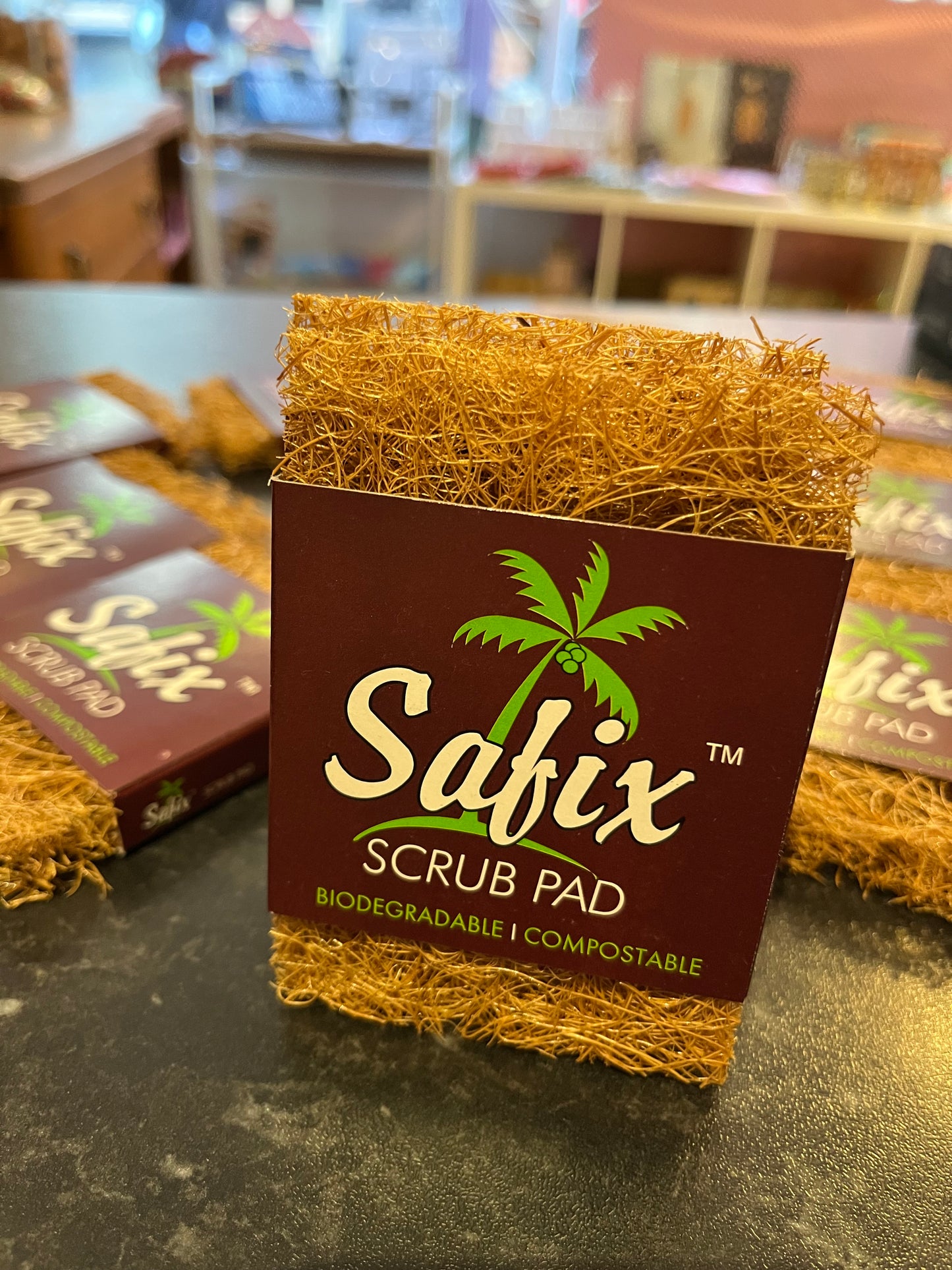 A coconut scrub pad or scourer. They have a brown card sleeve with a green palm tree with 'Safix scrub pad. Biodegradable. Compostable' printed in white and green.