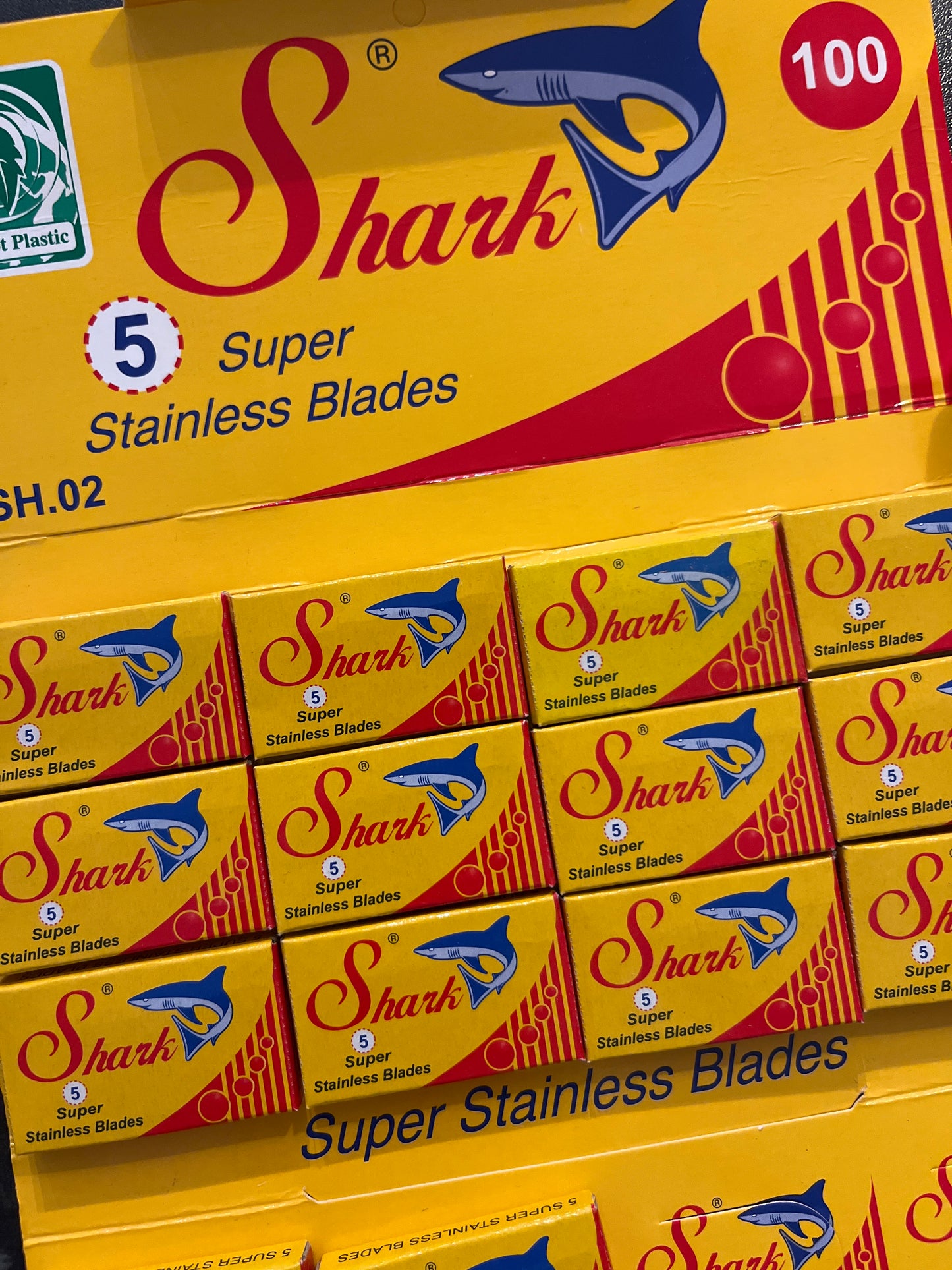 A brightly coloured red and yellow card holds multiple packs of razor blades each reading "5 Super Stainless Blades" and featuring a blue shark.