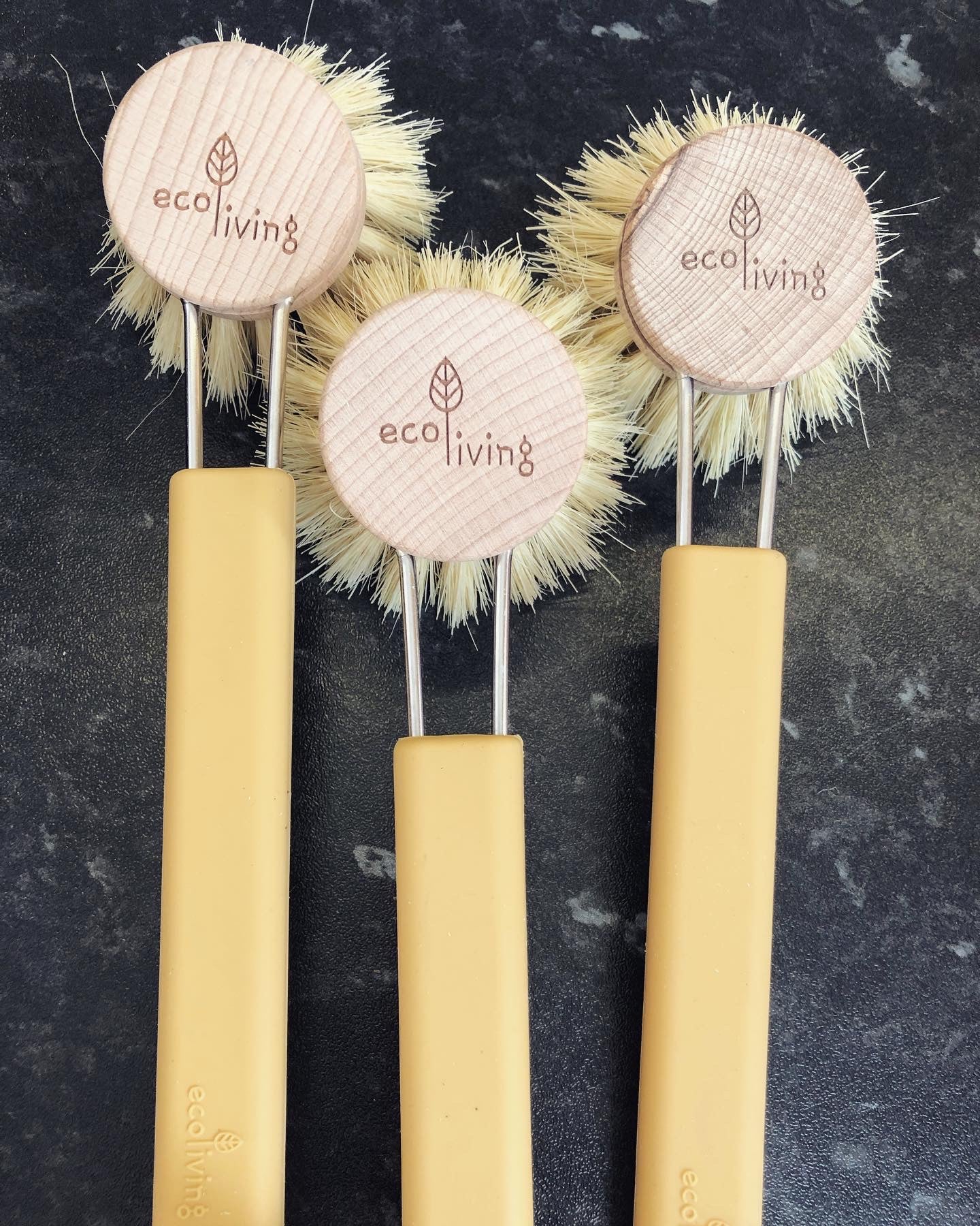 Three modern design washing up brushes with soft yellow silicone handles and replaceable wooden heads with natural bristles.