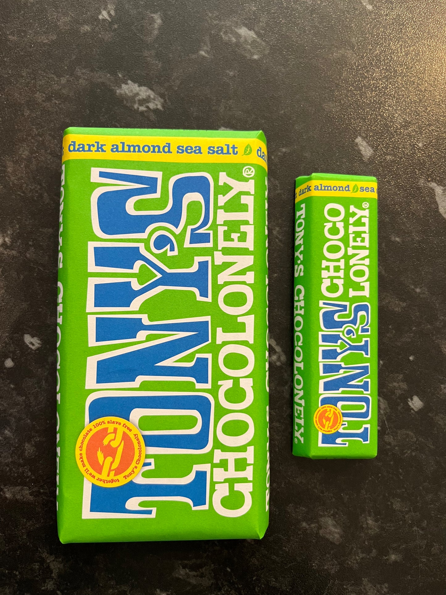 A Bar of Dark Sea Salt Almond Tony’s Chocolonely in green paper wrappers on a dark counter.