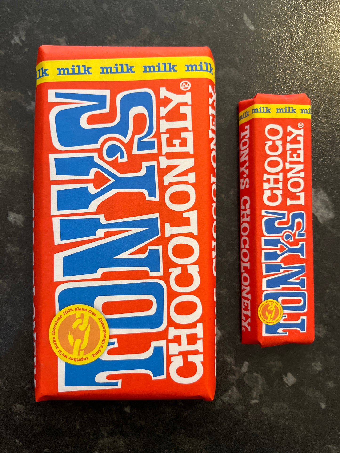 A large and small Milk Chocolate Tony’s bars in red paper wrappers side by side on a dark counter