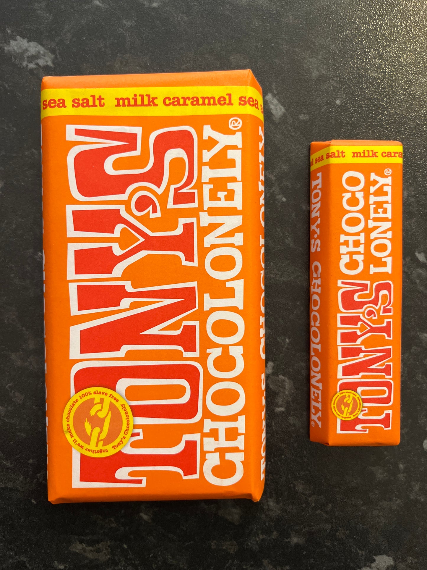 A large and small Sea Salt Tony’s bars in orange paper wrappers side by side on a dark counter