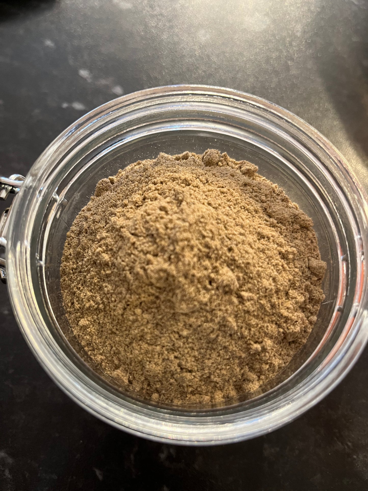an open jar of ground cardamom spice sits on a dark counter