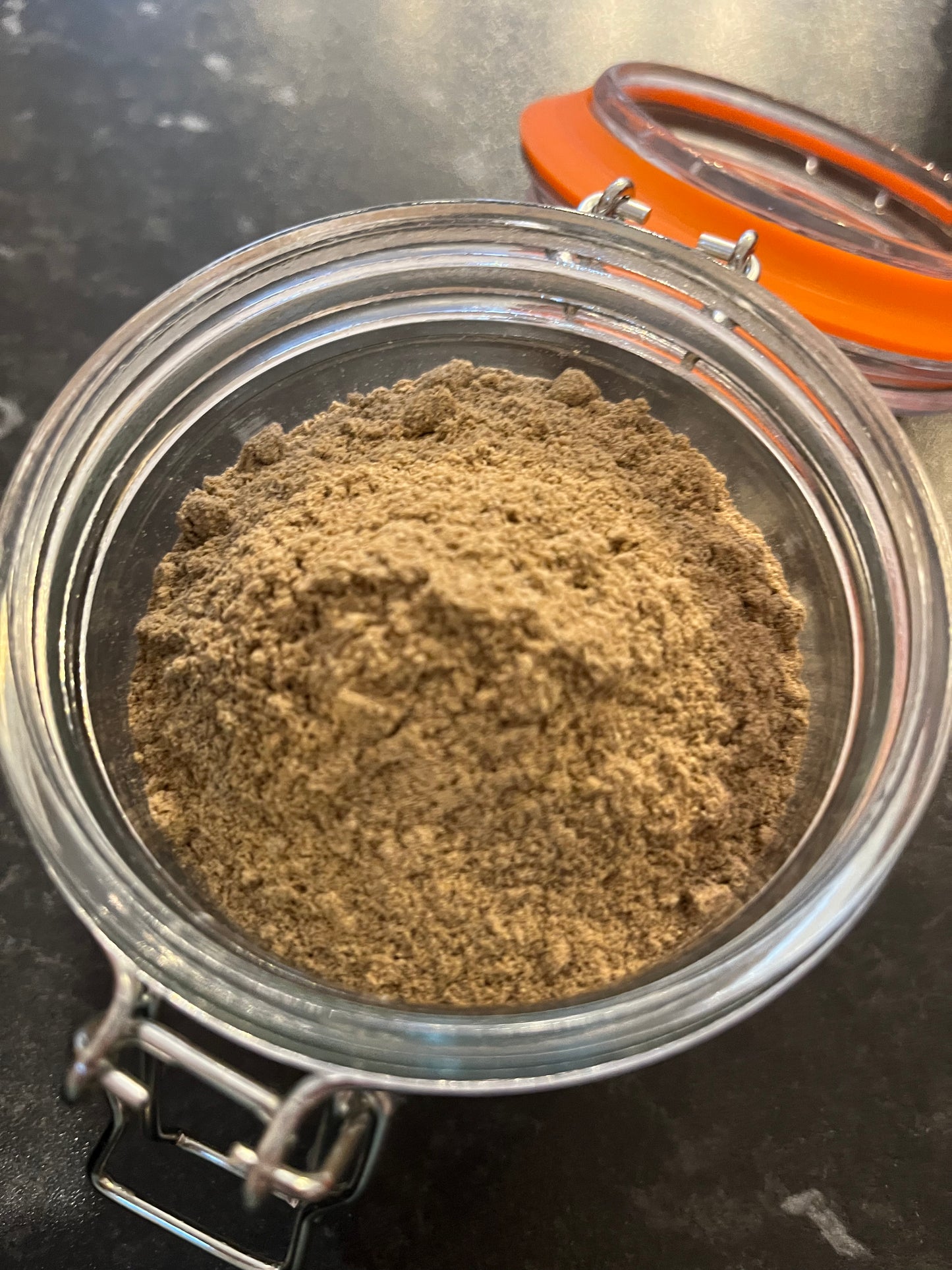 an open kilner jar contains finely ground and fragrant light brown cardamom powder.
