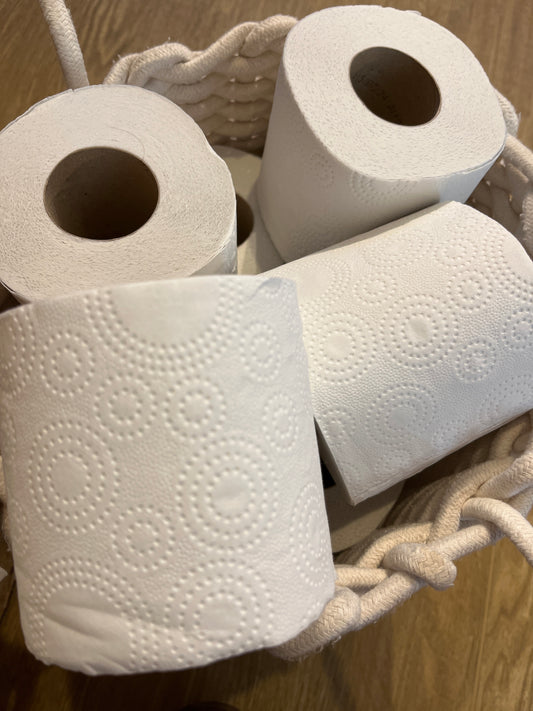 Packaging free rolls of white recycled toilet paper embossed with a circular design in a white cotton basket.
