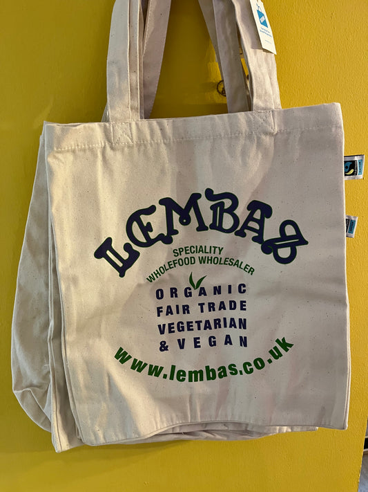 A natural cotton bag with wide shoulder straps, printed in dark blue and green to read ‘Lembas, Specialty Wholefood Wholesaler, Organic, Fairtrade, Vegetarian, & Vegan’
