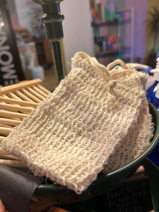 A number of cream coloured drawstring bags made from fibrous natural material rest alongside wooden soap racks in a shop display