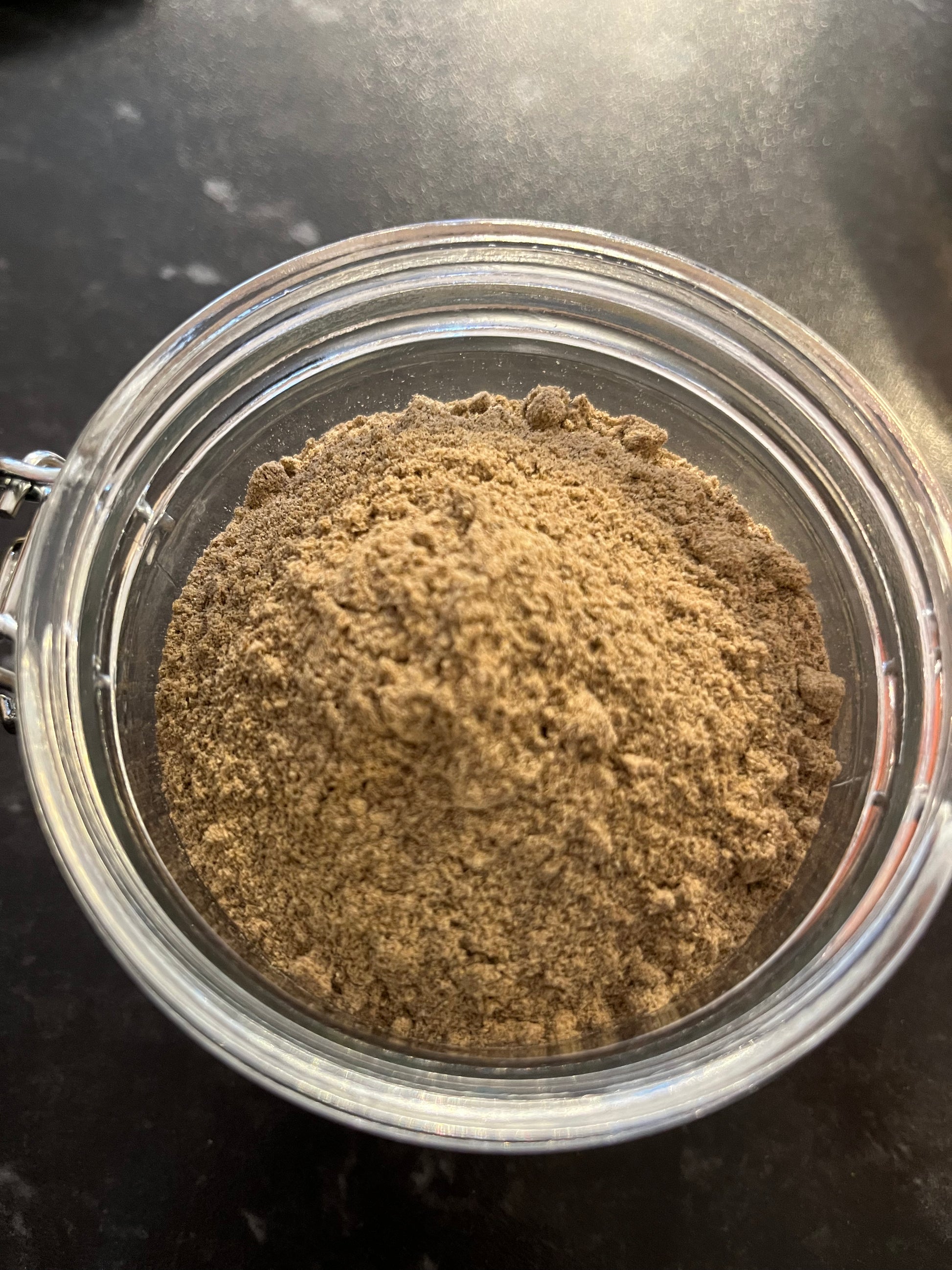 an open jar of ground cardamom spice sits on a dark counter